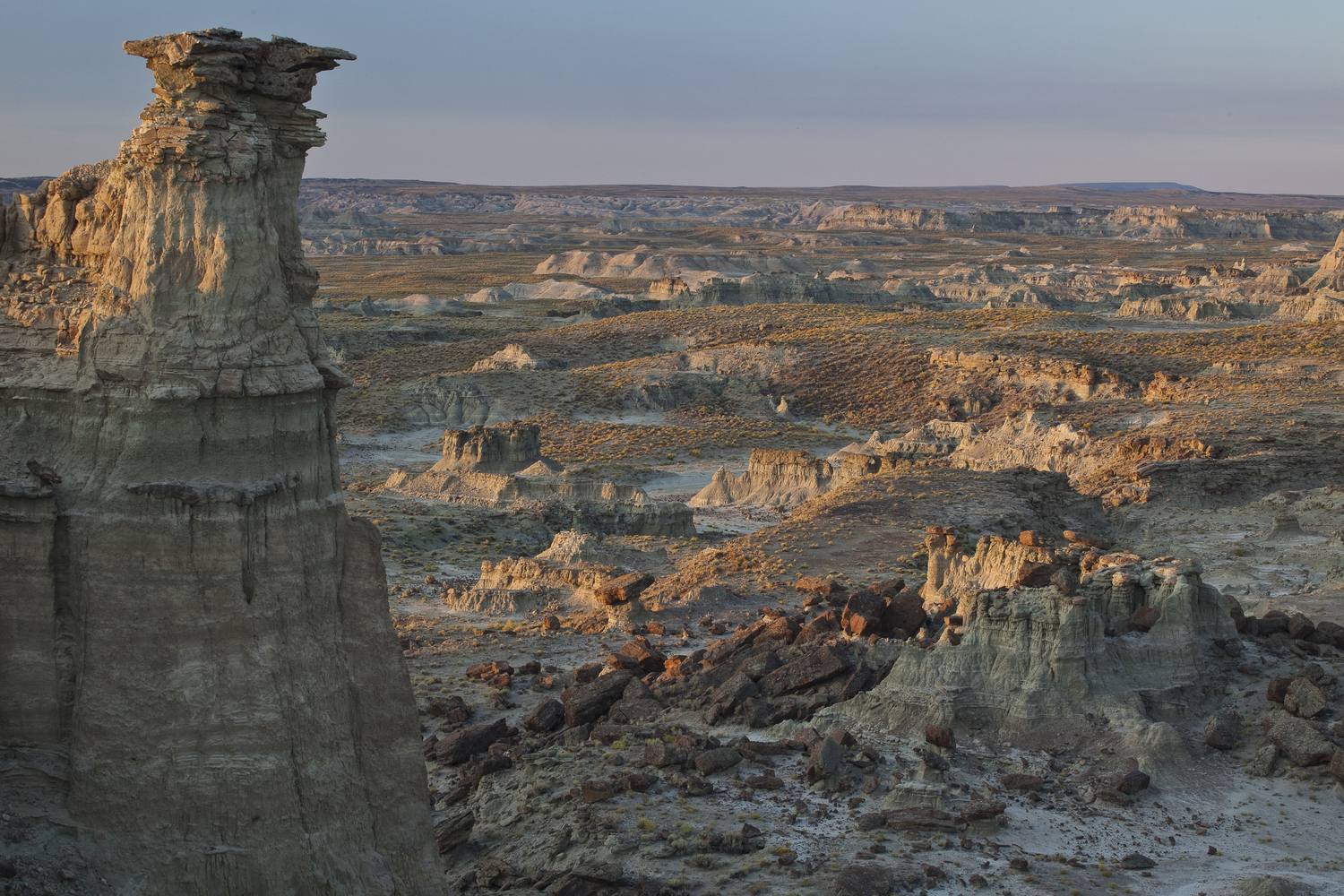A lone hoodoo standing over the eroded badlands of Adobe Town at dusk.